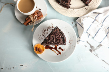 Plate with piece of delicious chocolate cake and cup of coffee on light table