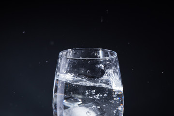 Glass of water on a gray background with drops in different directions