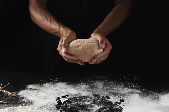 Man holding raw dough on black background