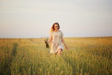 Fototapeta na wymiar girl with flowers walking on a grain field.