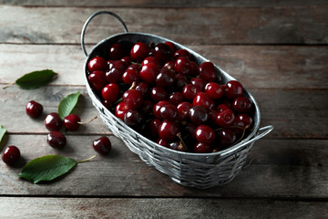 Metal basket with ripe cherry on wooden background