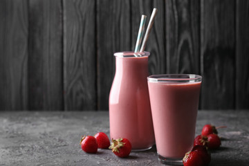 Glass and bottle with strawberry smoothie on grey table