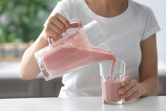 Woman Pouring Strawberry Smoothie From Jug Into Glass Indoors