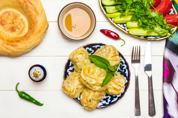 traditional Uzbek dish Manta with potatoes, meat and pumpkin, Uzbek ж, tomatoes and cucumbers on plates with national ornaments on a white wooden background