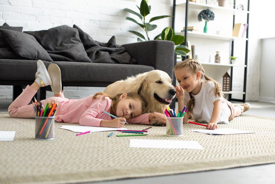 smiling kids lying on floor together with golden retriever dog at home