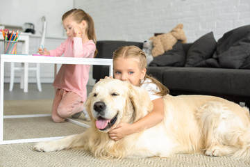 selective focus of kid hugging golden retriever dog on floor while sister drawing picture at home