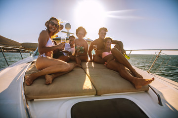 Group of friends sitting on the yacht deck with drinks - obrazy, fototapety, plakaty