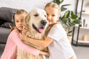 portrait of adorable smiling kids hugging golden retriever dog at home