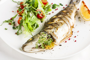 Baked fish with lemon and fresh vegetables on white plate