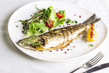Baked fish with lemon and fresh vegetables on white plate