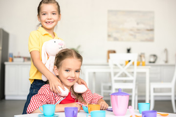 little smiling sisters pretending to have tea party together at home