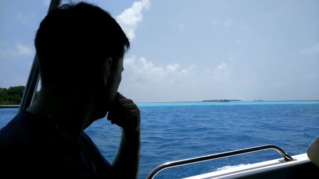 A man swims on a boat to a tropical island across the ocean.