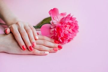 Creative bright trendy summer manicure with nails of different color. Female hands with art nail design on pink background and fuchsia peony flower.