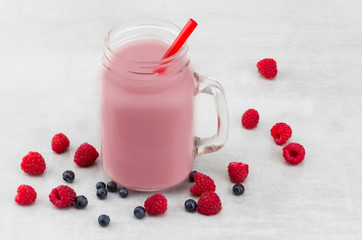 Beautiful appetizer pink raspberries and blueberry fruit smoothie or milkshake in glass jar with berries background. Yogurt cocktail. Close up.