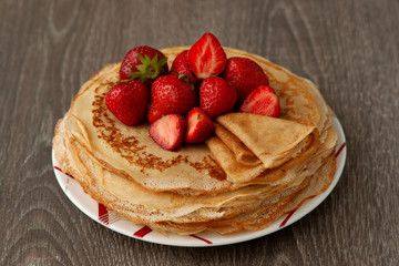 Pancakes with strawberries on a saucer. Thin baked pancakes with strawberry berries. Dessert for breakfast in the form of pancakes.