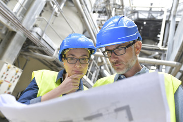 Industrial workers in factory checking blueprint