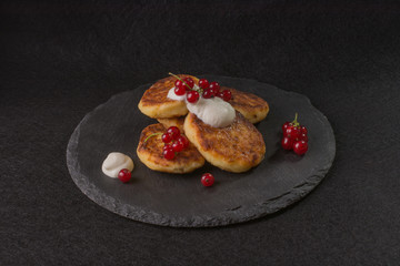 Cottage cheese fritters, pancakes with berries and sour cream on black shale 