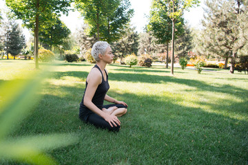 side view of woman practicing yoga in lotus pose on grass in park