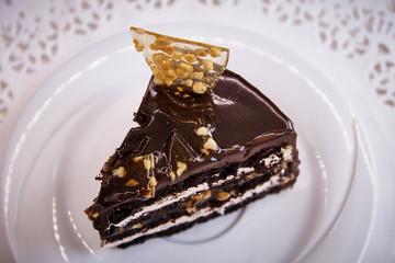 A piece of chocolate cake with caramel on a white plate with lace close-up.
