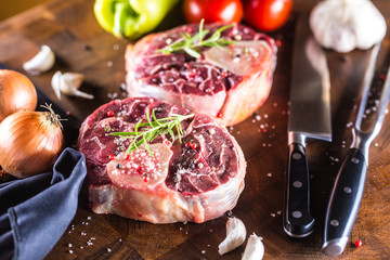 Two pieces raw beef shank and basic ingredients on goulash - onion pepper tomatoes garlic salt spices and rosemary