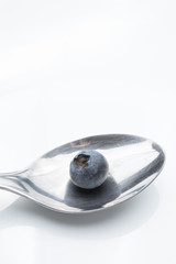 Black blueberry in a spoon on a white background