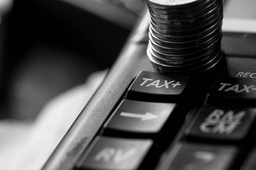 Tax word on used calculator, stack of coins, conceptual image of increasing taxes in black and white.