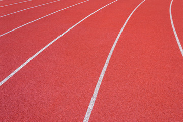 Fototapeta premium White lines of stadium and texture of running racetrack red rubber racetracks in outdoor stadium are 8 track and green grass field,empty athletics stadium with track,football field, soccer field.
