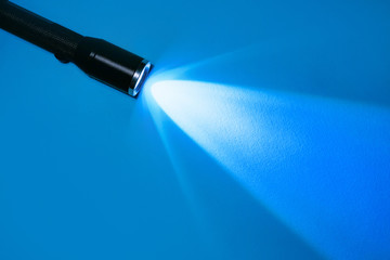 flashlight and a ray of light in the dark on a blue background. A modern LED lamp with a bright projection. Surface with a copy. - obrazy, fototapety, plakaty