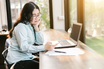 Business Asian woman be dressed in earphone working with smartphone and laptop computer on in coffee shop like the background.