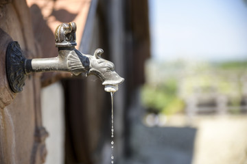 rustic old water tap in foreground of village - obrazy, fototapety, plakaty