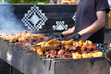 Man in black T-shirt roasting marinated meat on grill. Street food and outdoor cooking concept