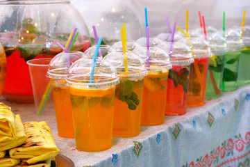 Summer bright drinks with lemon slices, mint and sparkling water in plastic cup with straw. Street food and outdoor cooking concept.