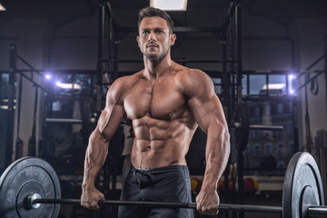 Fototapeta na wymiar Young handsome sportsman bodybuilder weightlifter with an ideal body, after coaching poses in front of the camera, abdominal muscles, biceps triceps. In sportswear.