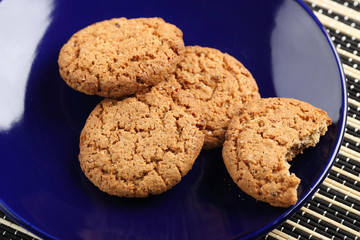 A bitten cookie on a plate. A lot of oatmeal cookies on a blue plate. View from above.
