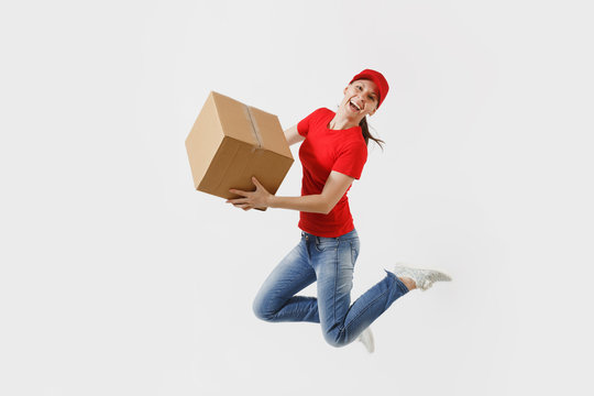Full length portrait of fun delivery woman in red cap, t-shirt isolated on white background. Female courier or dealer jumping with empty cardboard box. Receiving package. Copy space for advertisement.