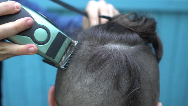 Barber woman cuts the hair of the client with electric razor clipper and comb on nape