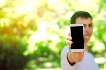 young european guy holding a smartphone in his hand. telephone dependence, social networks. work on the Internet. write message. sunny day. nature, open air. close-up, space for text.