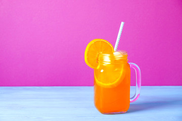 Colorful composition with vintage mason jar glass full of fresh orange juice based non alcoholic summer iced cocktail, straw, fruit, blue wooden table, pink background. Close up, copy space, top view.
