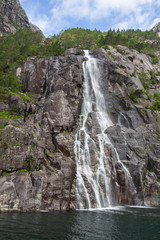 Water falls from steep rocks and disperse into spray veil on the mountain slopes beside Lysefjord, Rogaland, Norway