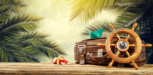 Summer suitcase of brown color and background of exotic palms 