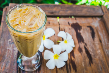 A coffee glass in the garden with white plumeria flowers on wooden floor.