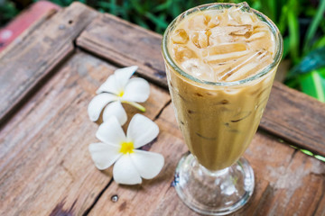 A coffee glass in the garden with white plumeria flowers on wooden floor.