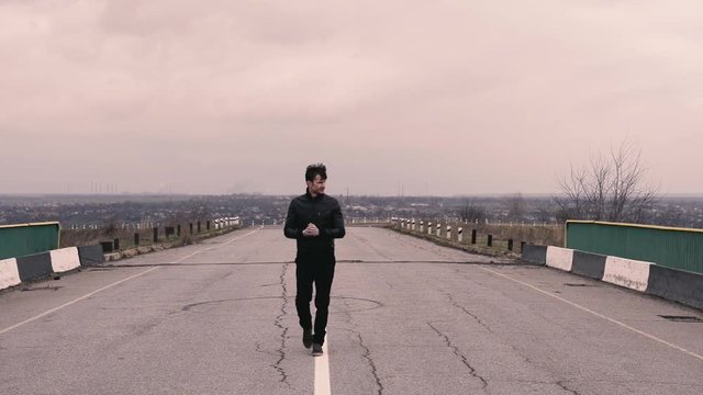 man smiles affably and walks along the road towards the camera.