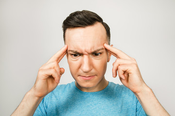 Young thinking man dressed in a blue t-shirt wiht fingers at head on a light background.