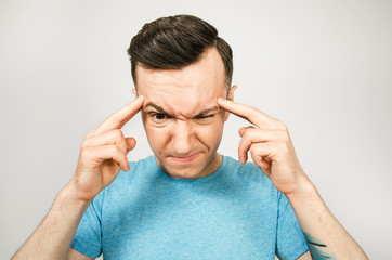 Young thinking guy dressed in a blue t-shirt wiht fingers at head on a light background.