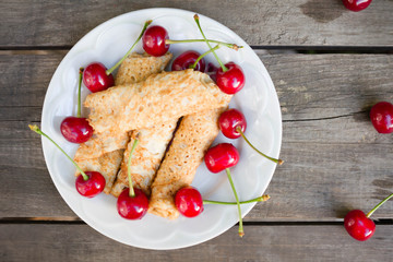 Homemade thin pancakes with cherries on a wooden table