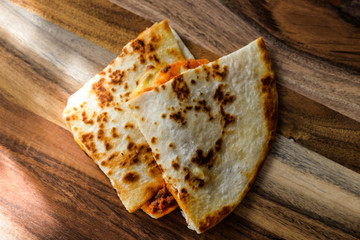 Two pieces of hot tasty quesadillas with cheese on a wooden cutting board for cafe, shop, menu, prints, market, advertising. Freshly baked tortillas with cheese and beef close up. Cake, tortilla.