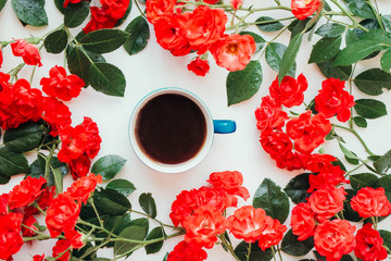 bright red small roses scattered around a cup of coffee, top view