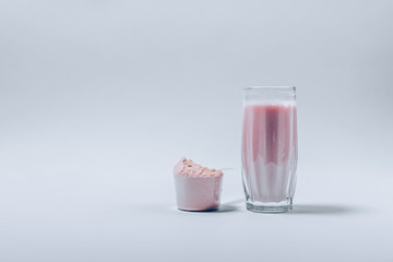 Glass of whey protein shake next to scoop of powder