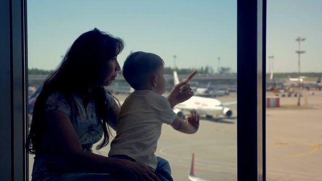 Son and mother sit in the airport looking to the airplanes.